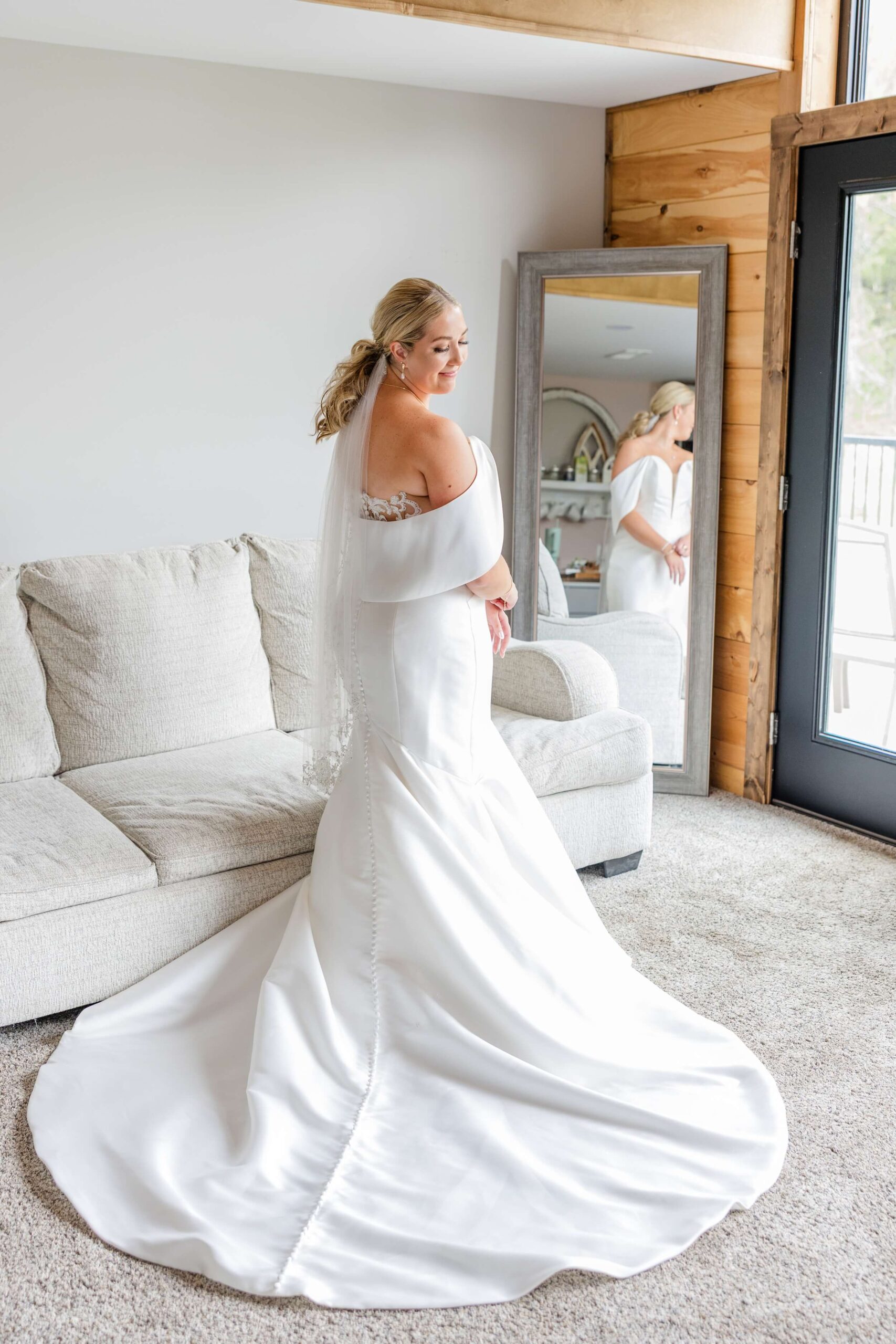 A bride admires her train while standing in a mirror in the getting ready room