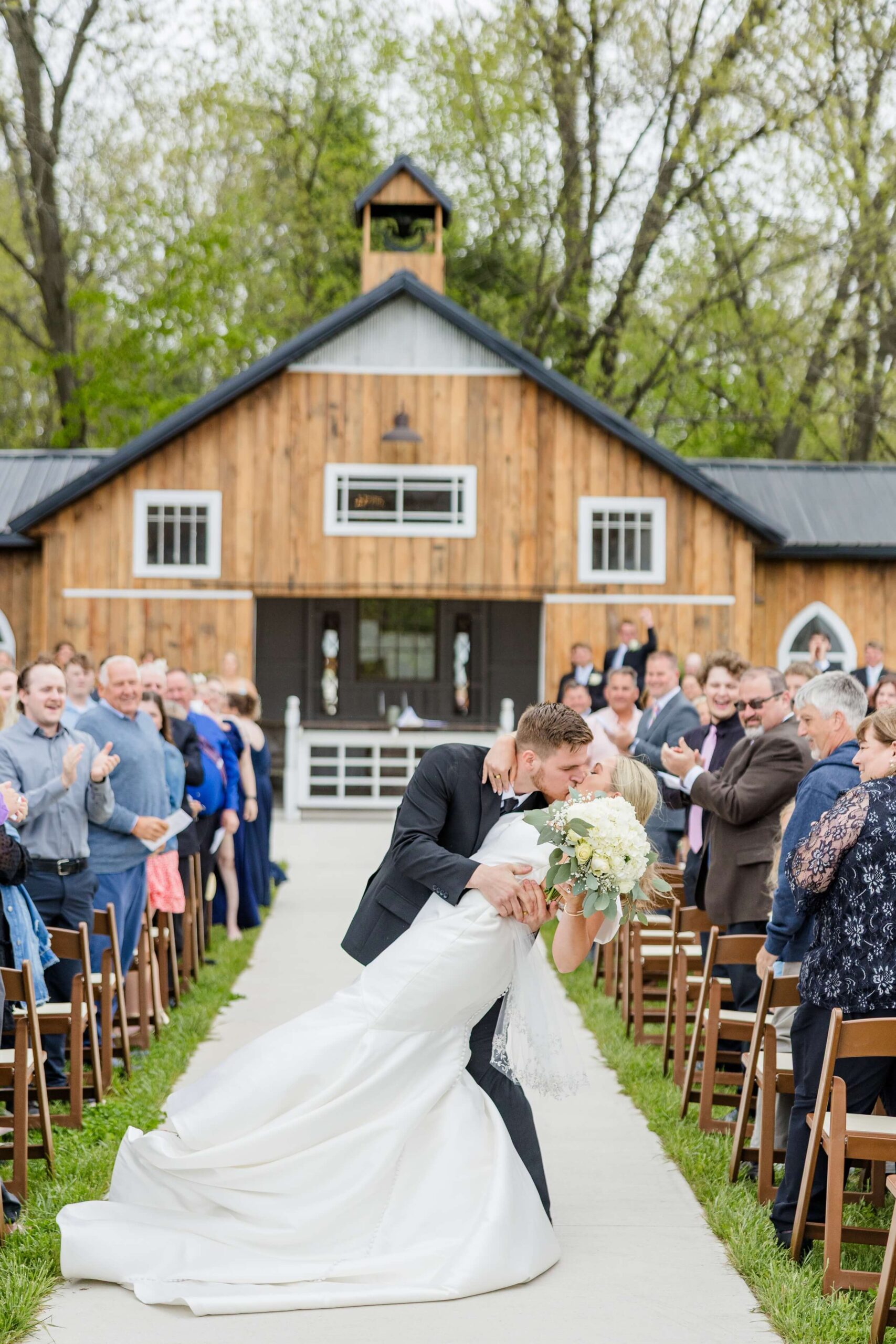 A groom dips his bride for a kiss to applause while exiting up the aisle at The Glenn Royal Barn Venue