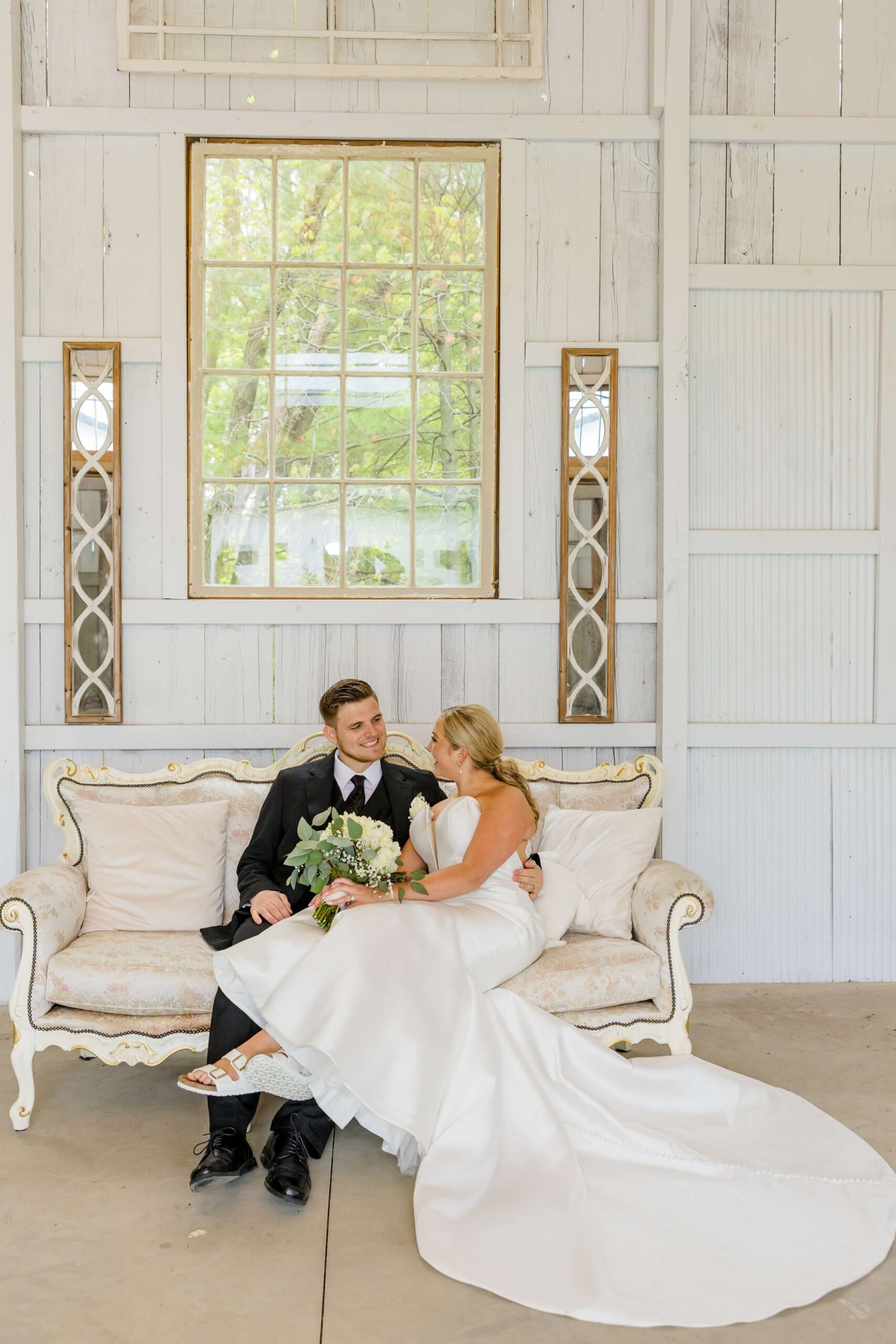 Newlyweds cuddle on an antique couch while smiling at each other