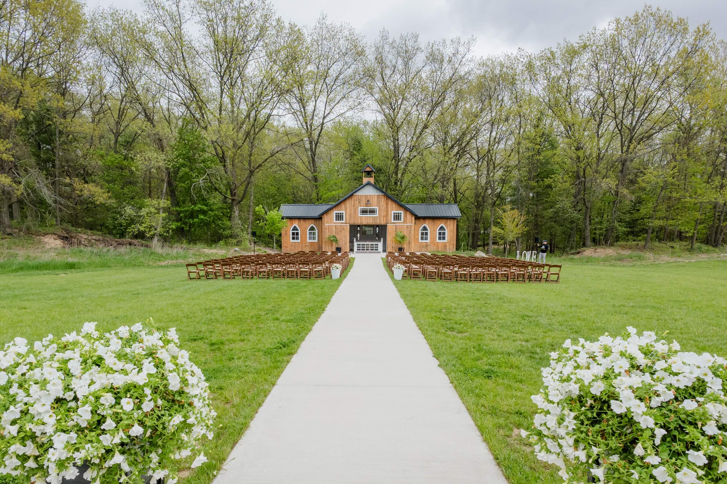 A look down the aisle towards the chapel of The Glenn Royal Barn Venue with an outdoor ceremony set up with wooden chairs