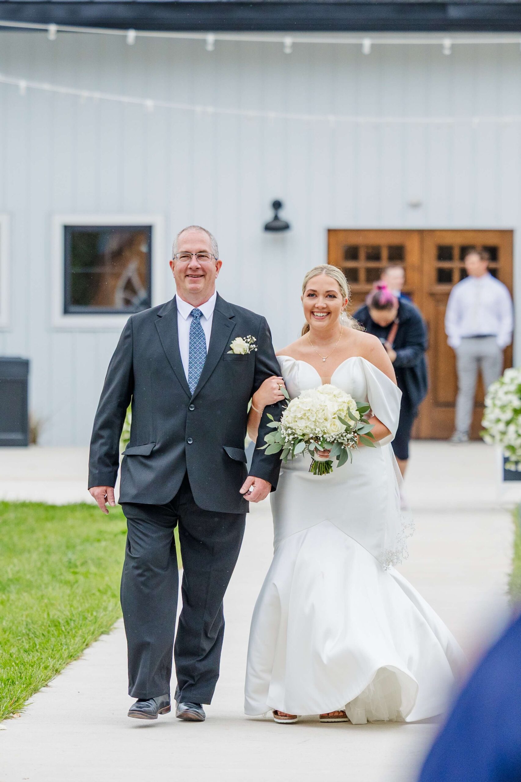 A happy bride is escorted down the aisle by her father in a grey suit
