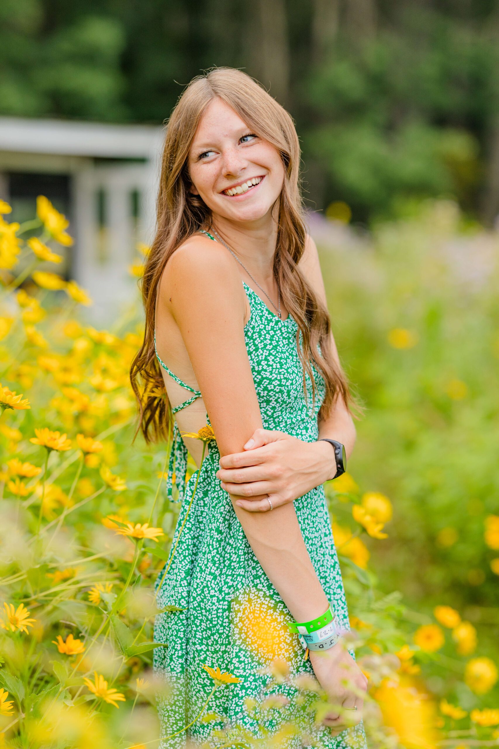 A laughing high school senior explores some yellow wildflower fields in michigan in a green dress