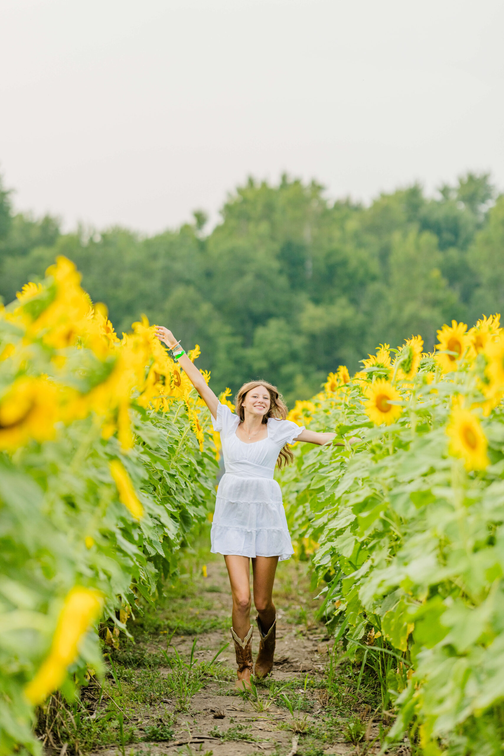 A teenage girl in a white dress frolics in some wildflower fields in michigan filled with sunflowers