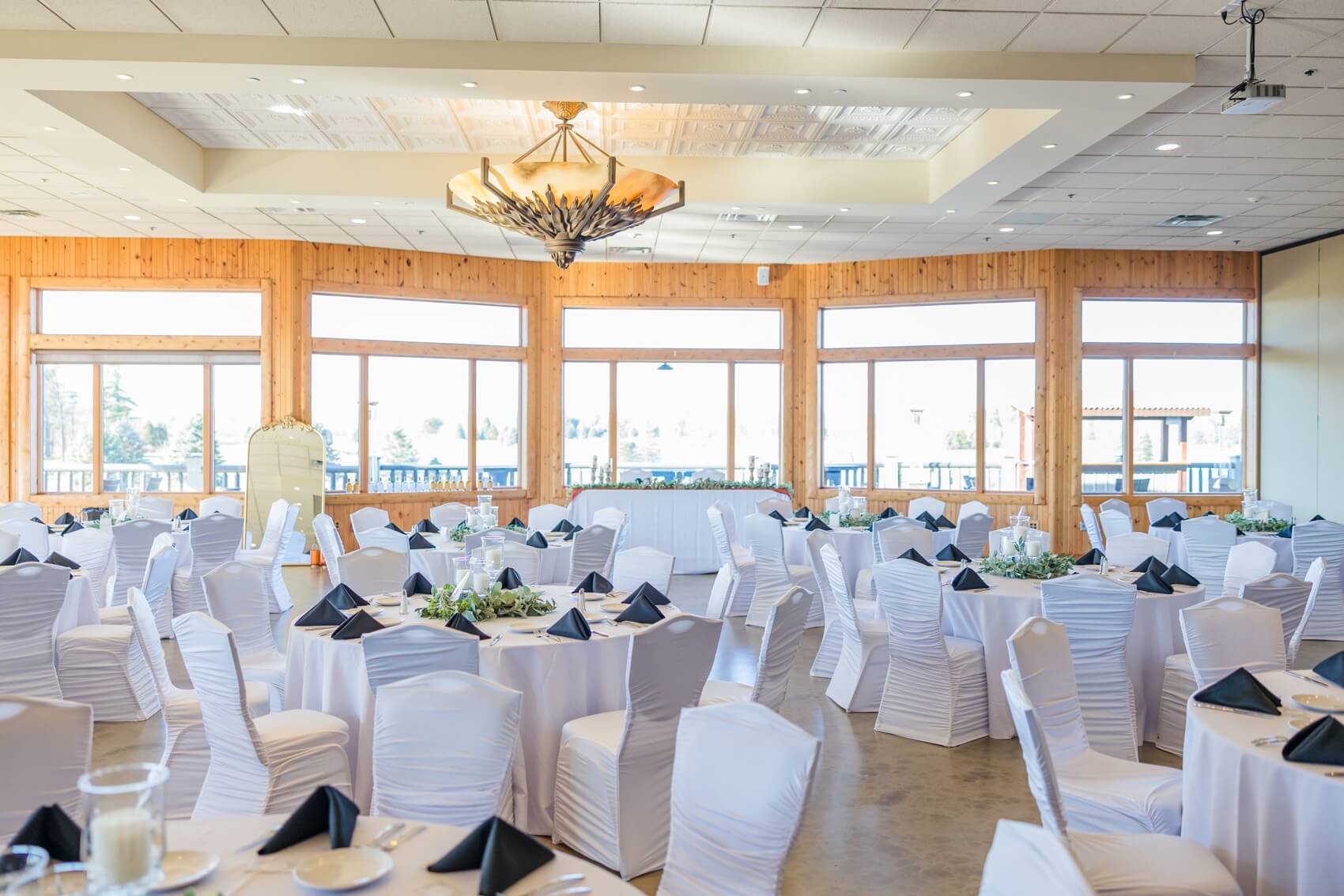 a look at an indoor wedding ceremony set up with white covered chairs and tables
