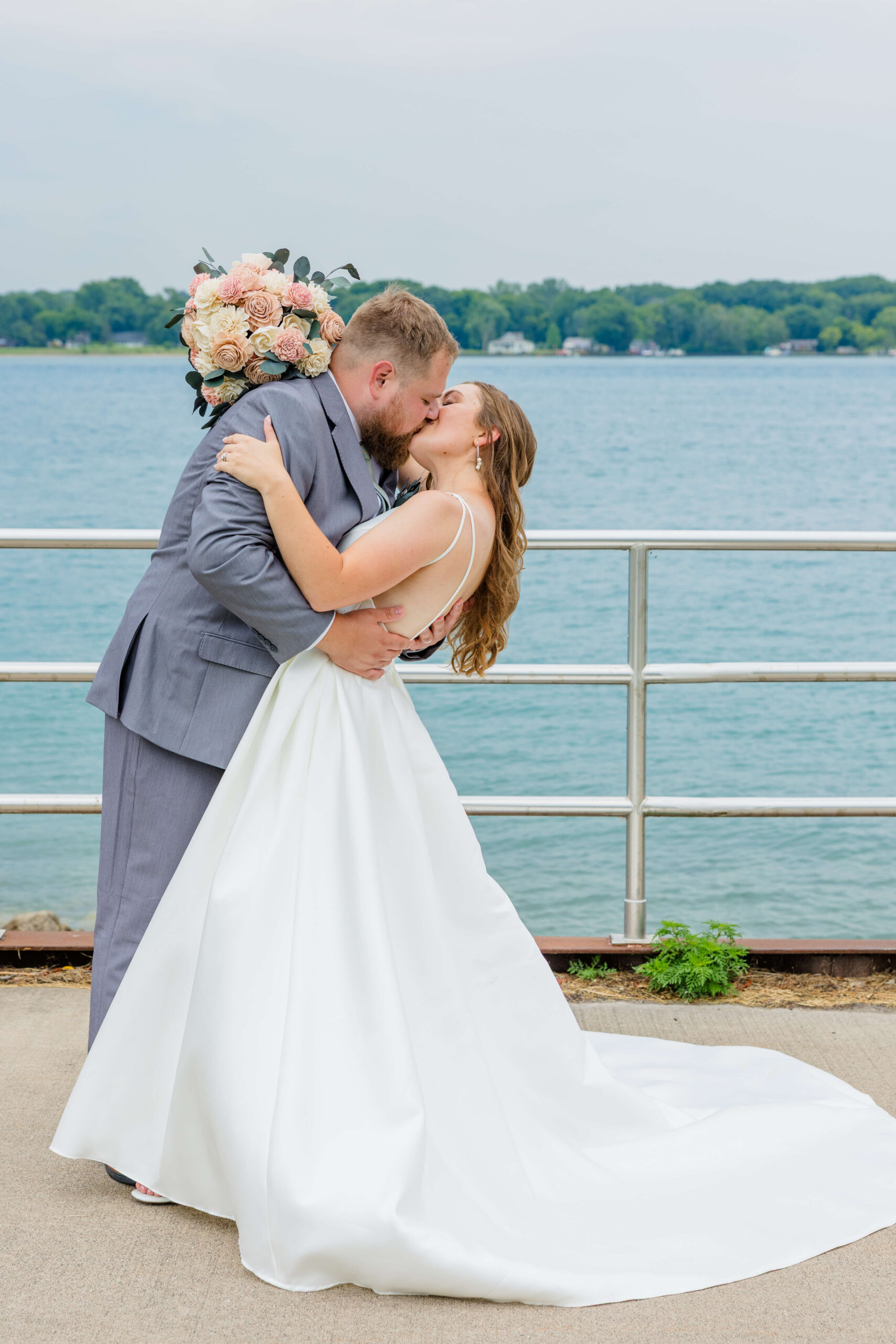 Newlyweds kiss and dip by the water during their alexanders banquet hall wedding