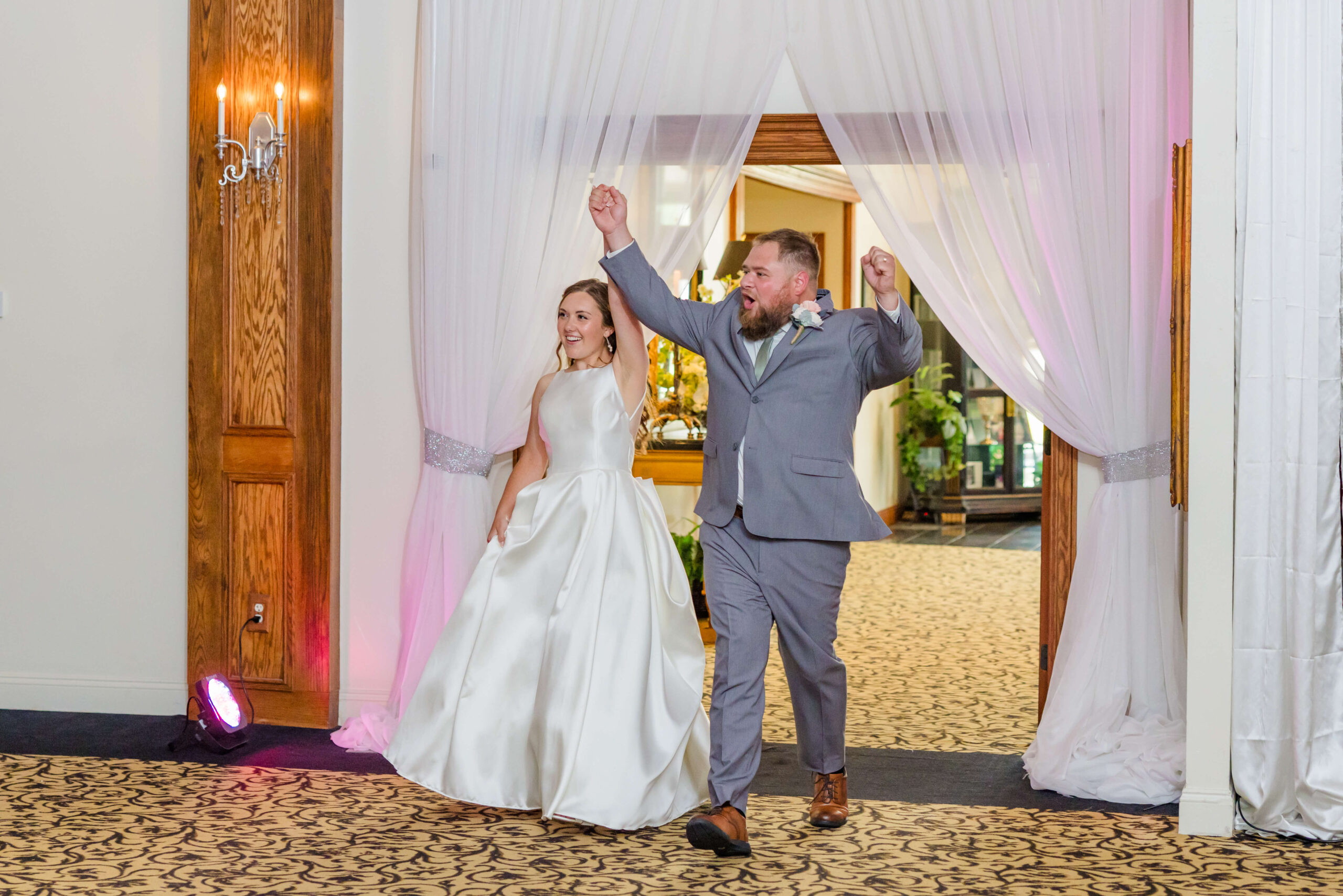 A bride and groom enter their alexanders banquet hall reception with hands up