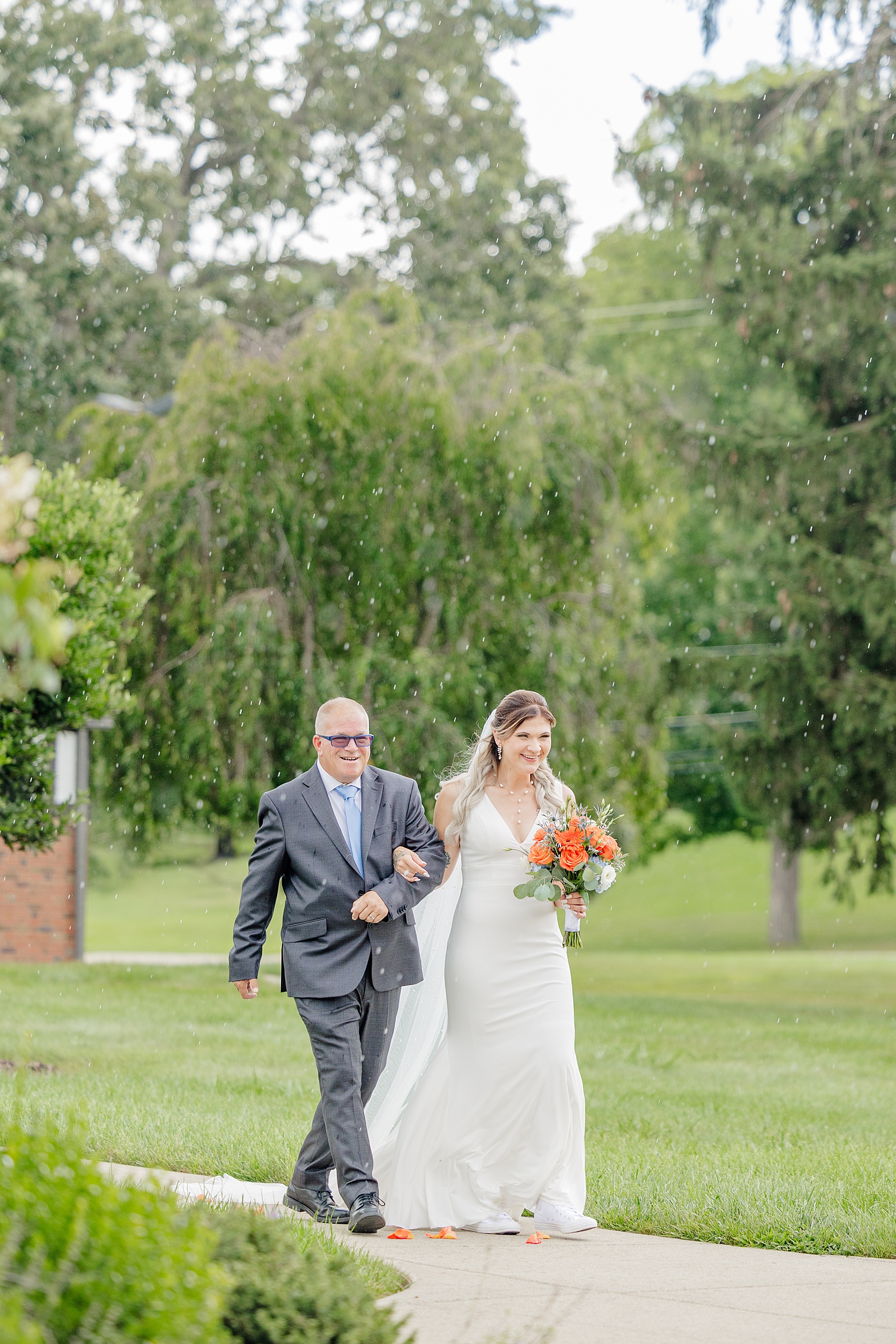 A bride walks down the aisle with dad in a light rain