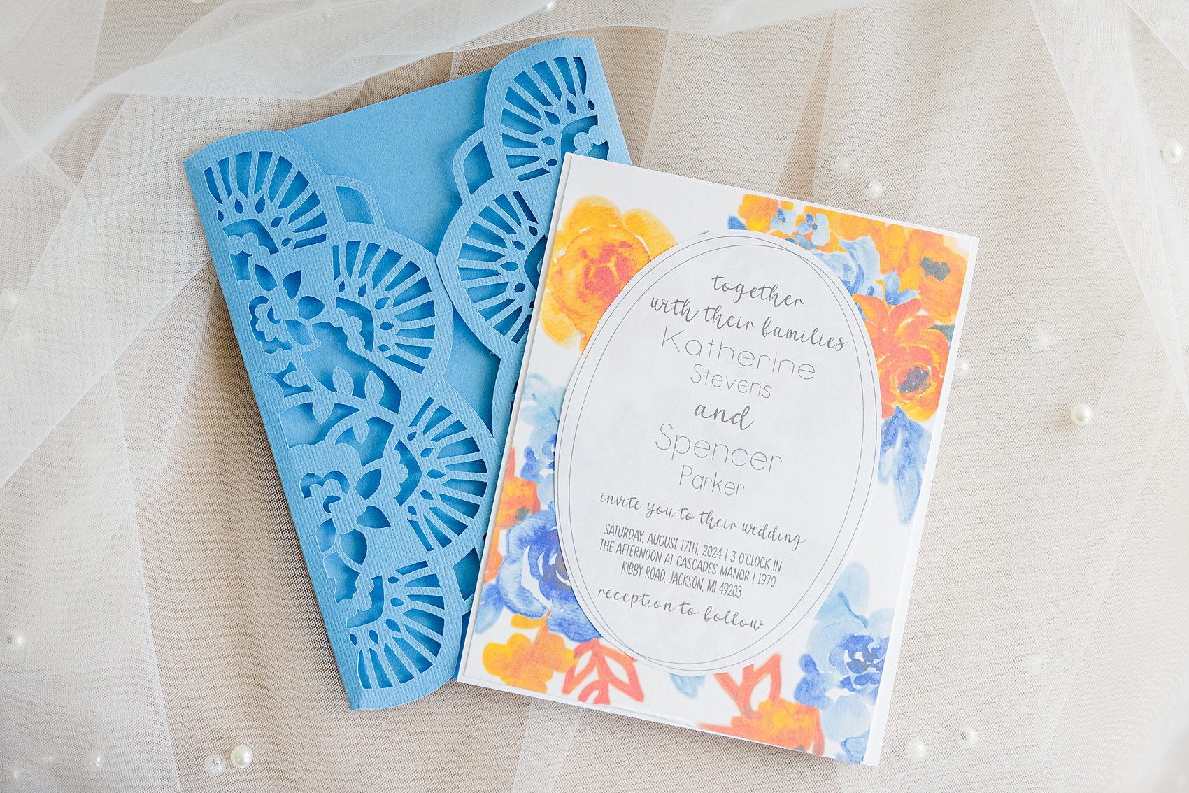 Details of blue and orange wedding invitations on a pearl covered veil