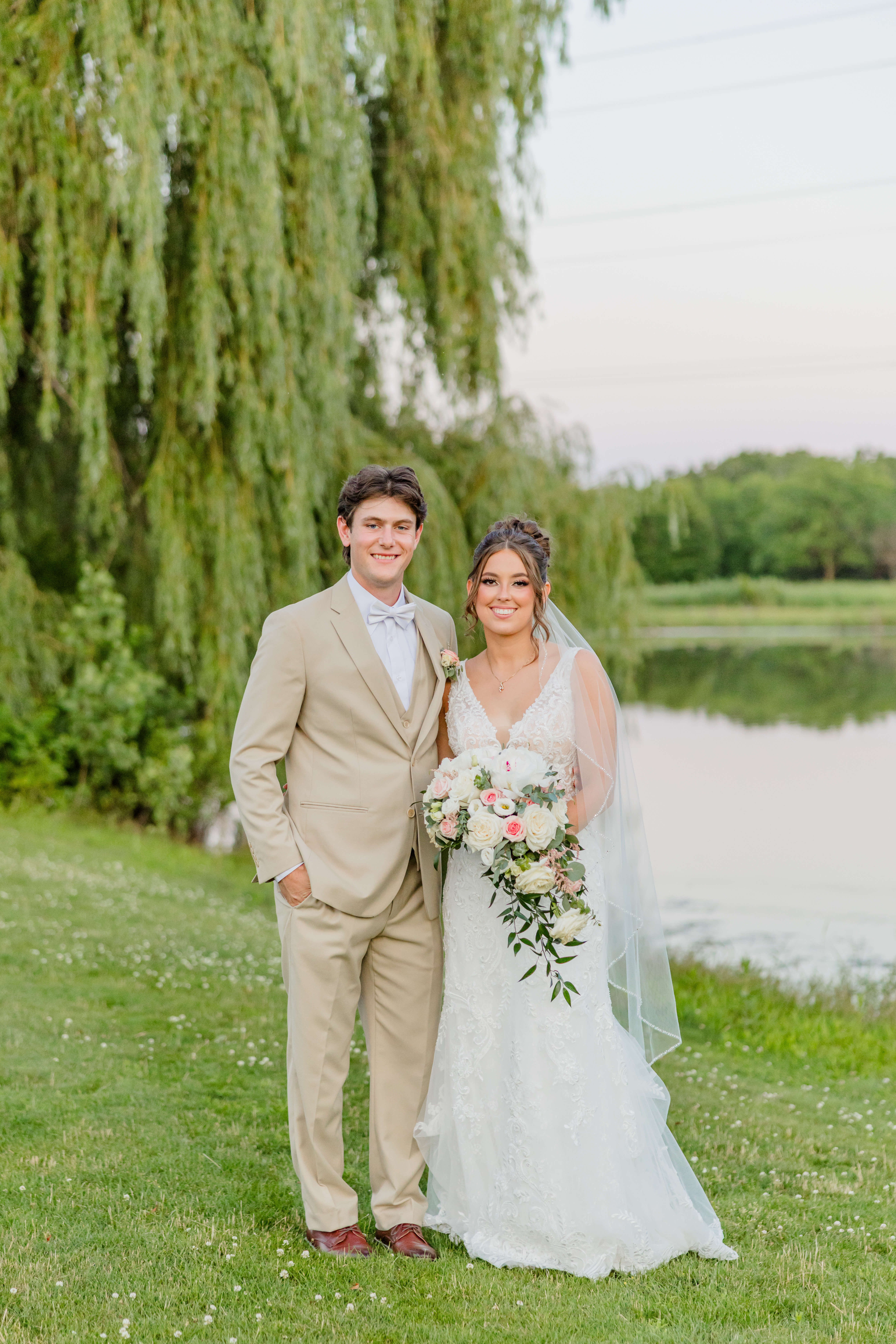 Newlyweds smile while standing by a pond during their golden hawk golf course wedding