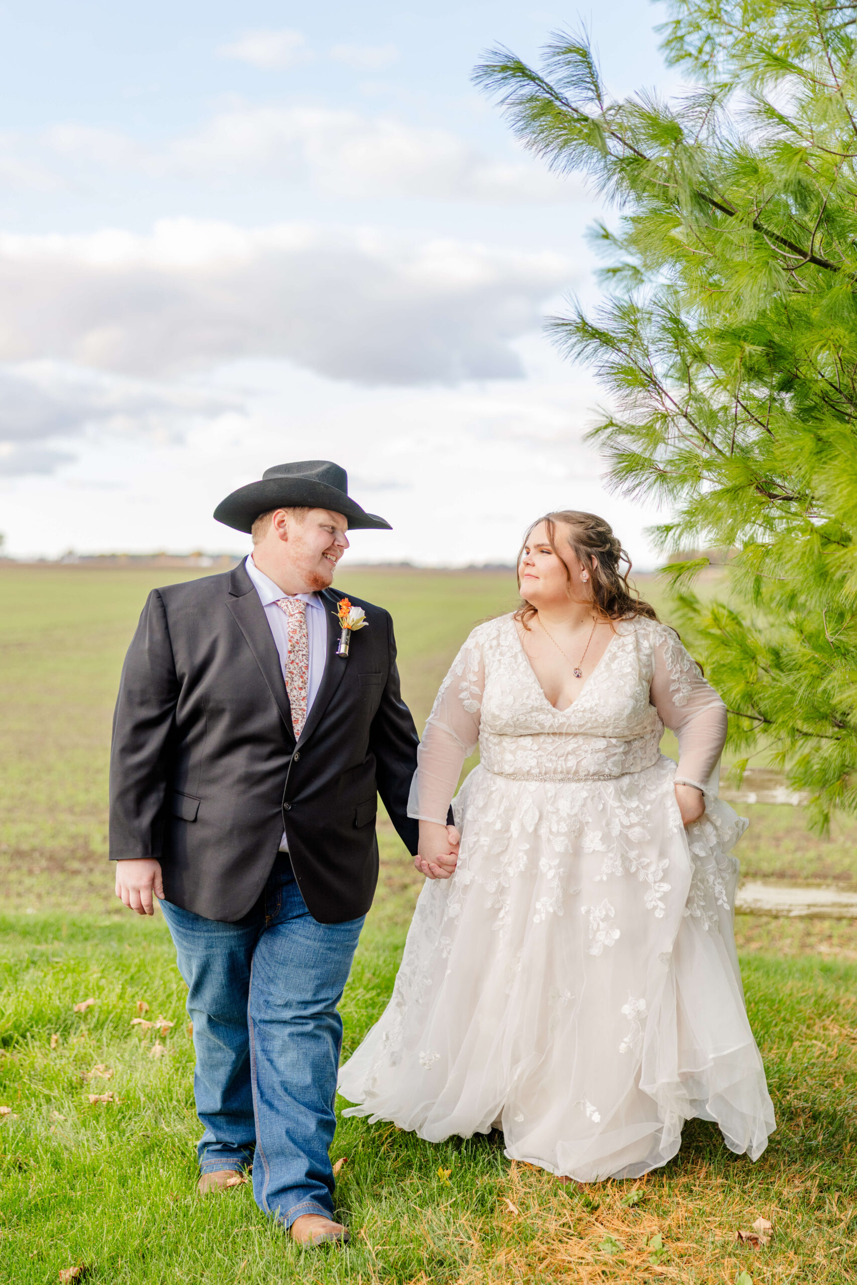 Newlyweds walk in a meadow holding hands and smiling at each other