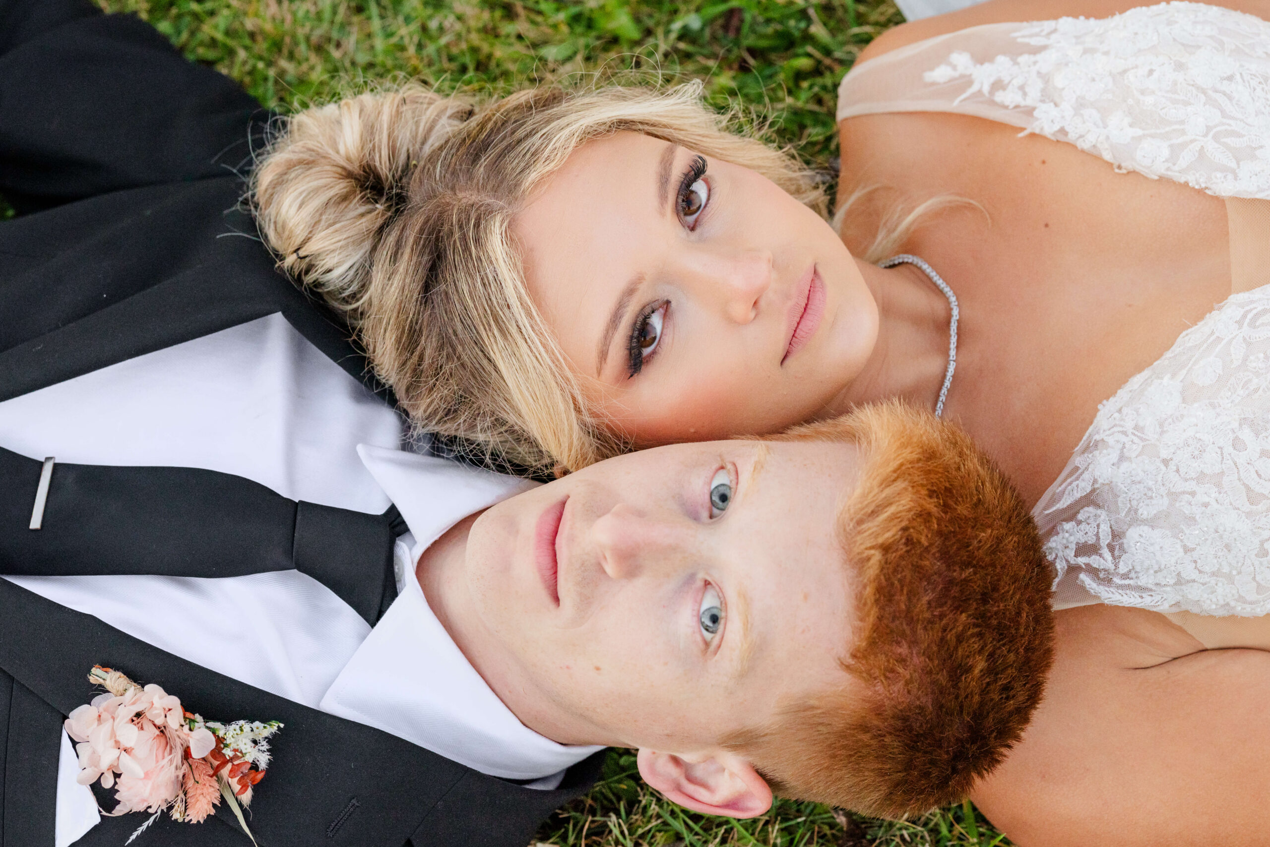 A bride and groom lay cheek to cheek in the lawn
