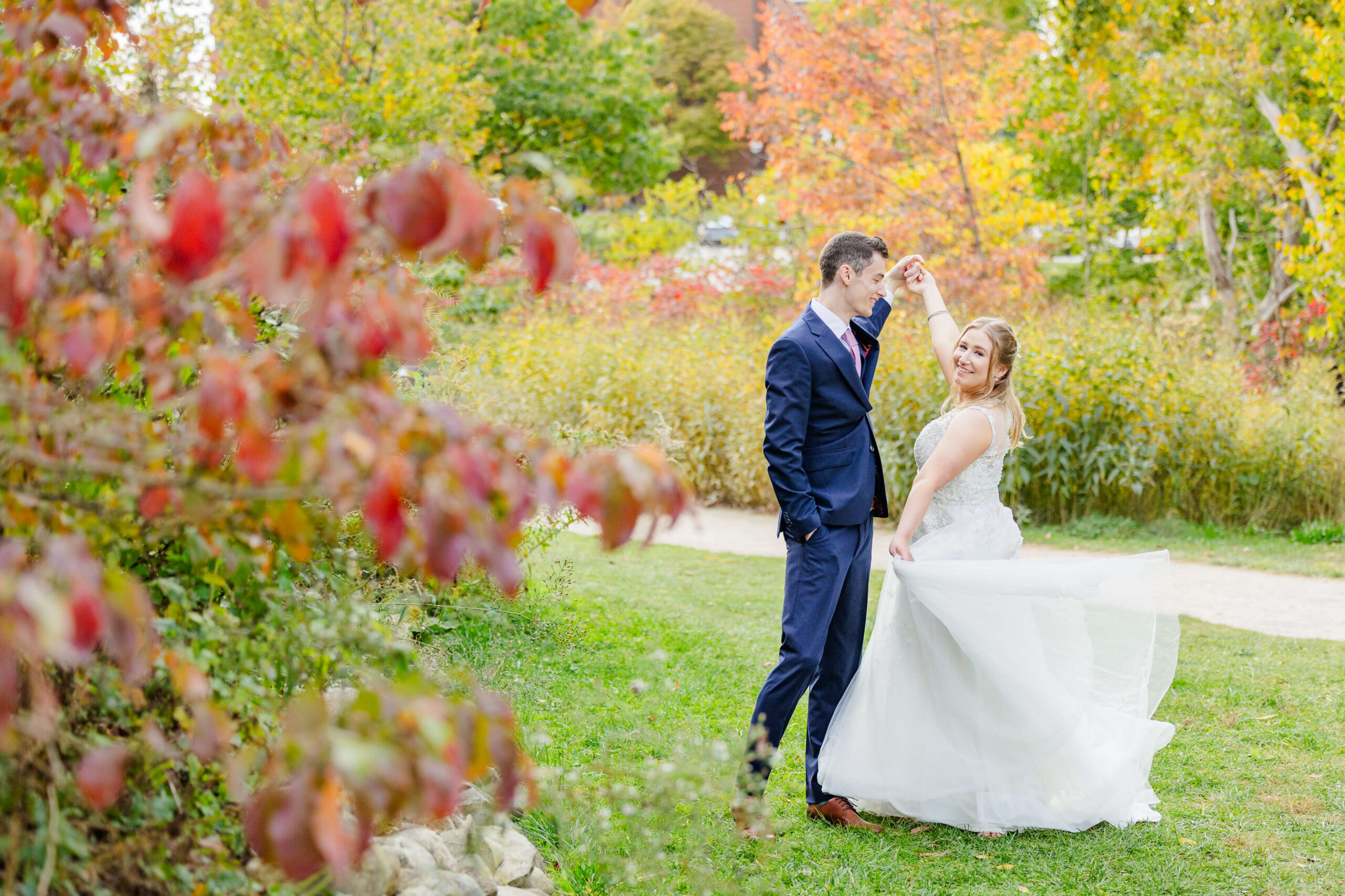 A happy newlywed couple dances in a garden with big smiles in fall at sunset