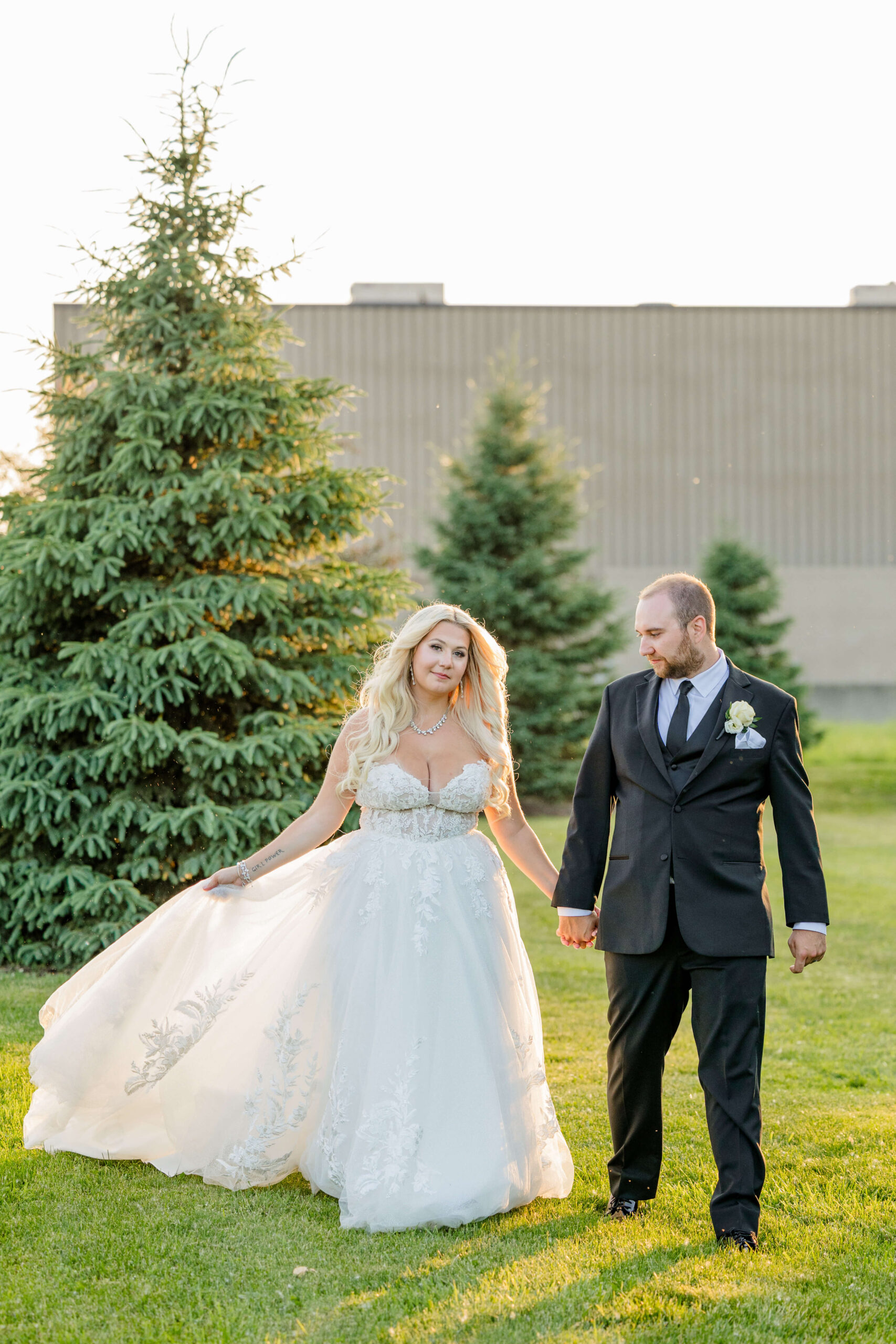 A bride and groom walk through pine trees at susnet holding hands at one of the ann arbor wedding venues