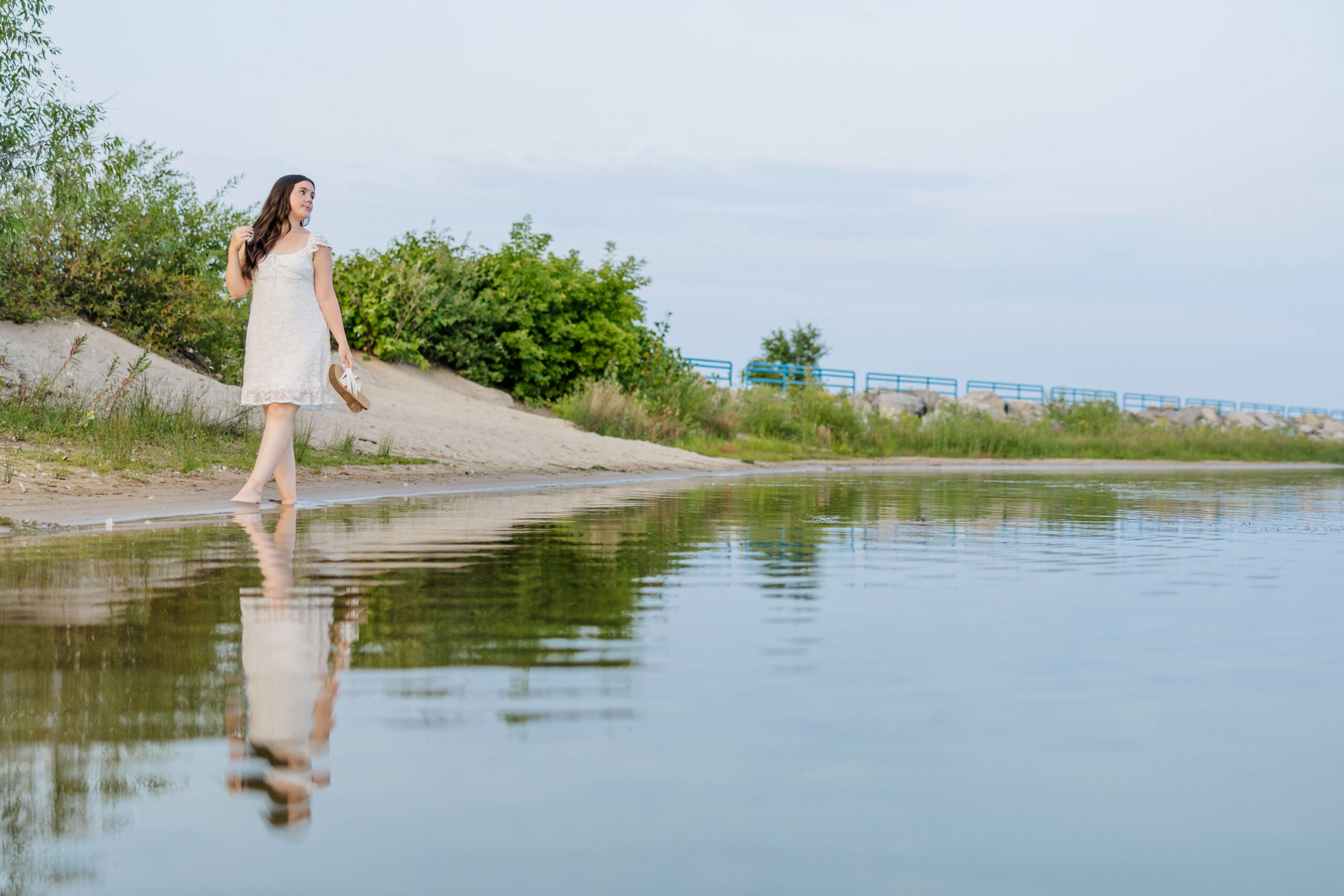A happy woman walks on a beach twirling her hair and carrying her shoes