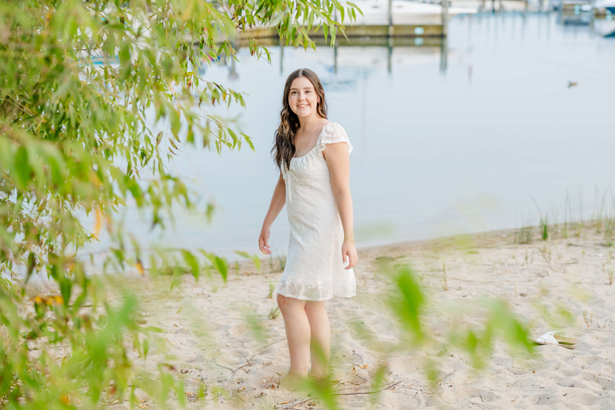 A woman walks on a beach in a white dress by the marina with a big smile