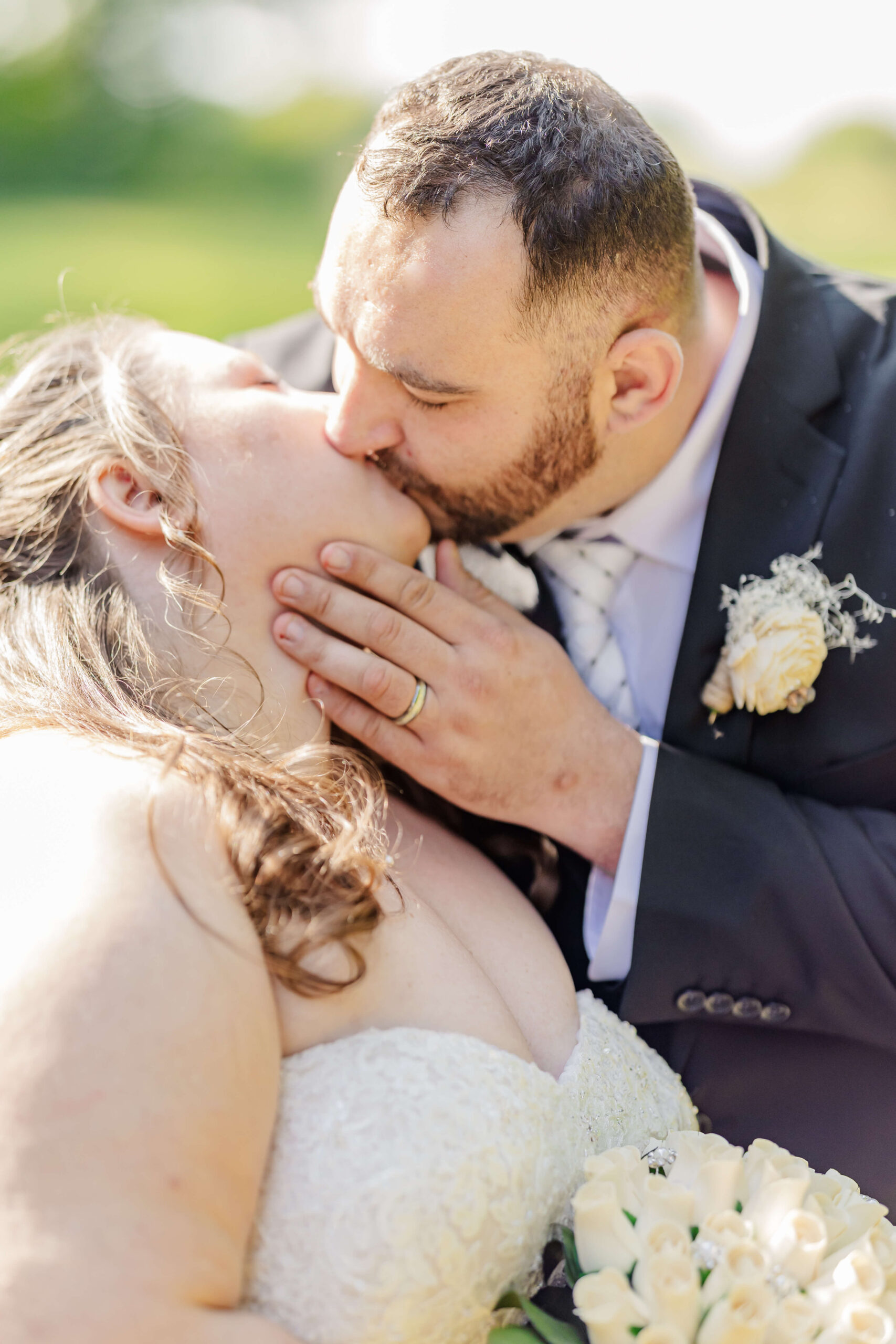 A bride and groom kiss in a field in the sun during their dunham hills country club wedding