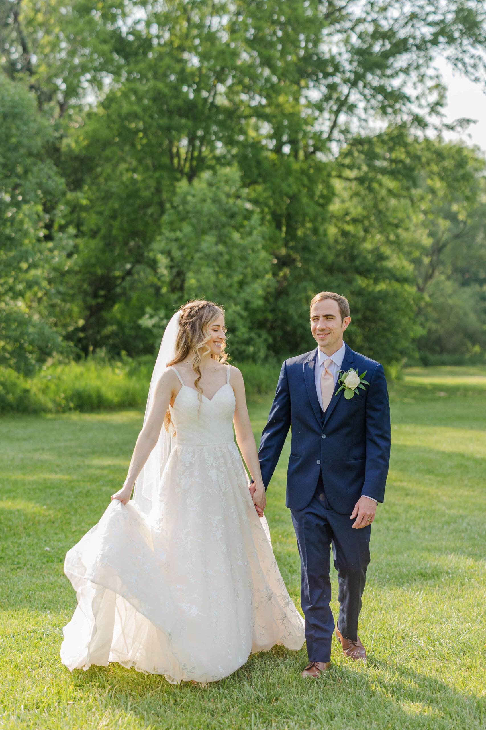 A happy newlywed couple walk in a lawn holding hands and smiling during their paint creek country club wedding