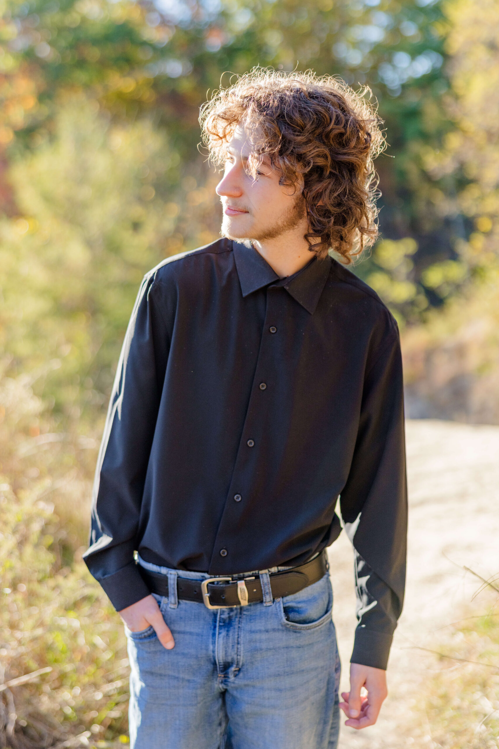 A high school grad walks with a hand in his pocket in a forest trail at sunset