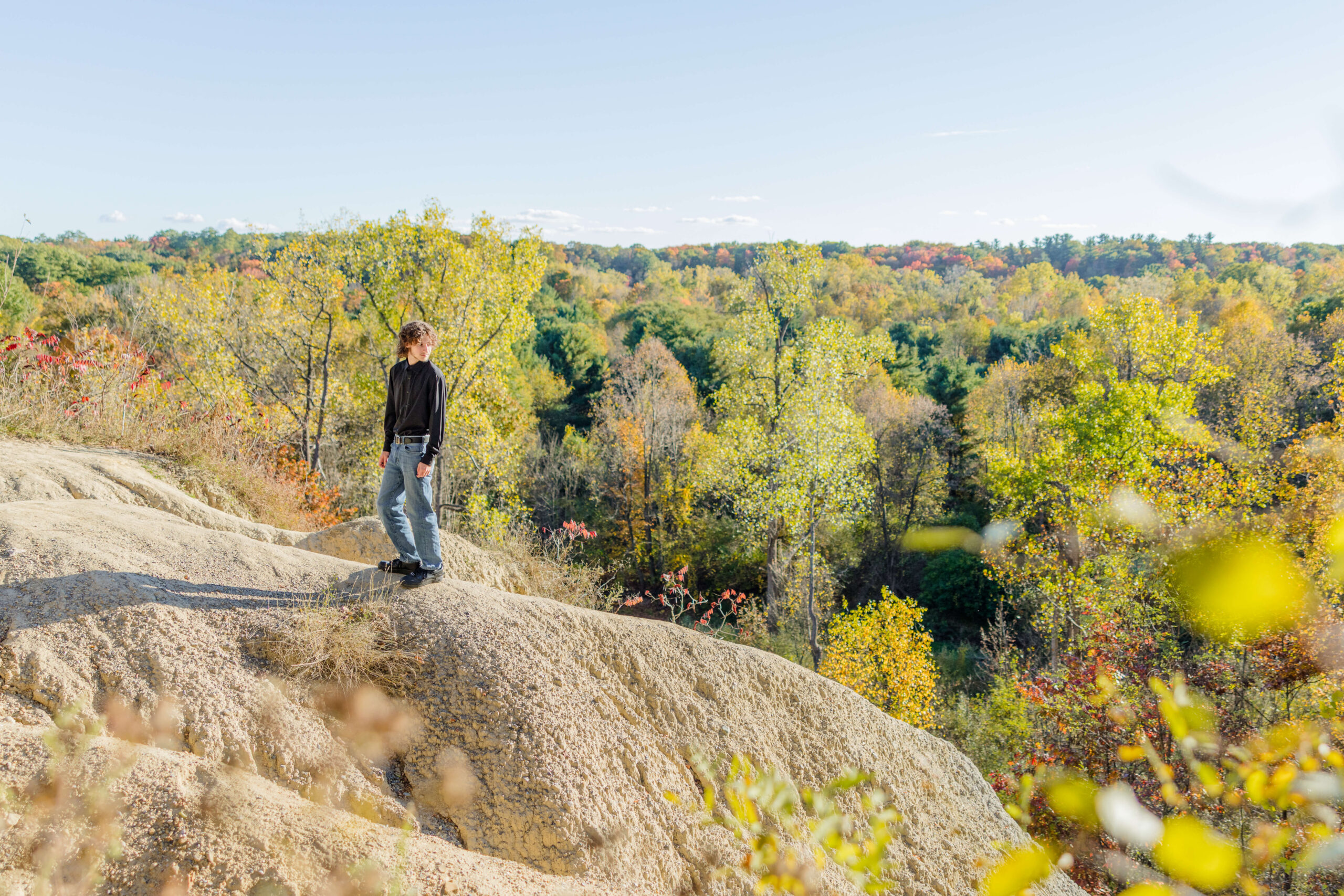 A high school senior stands on a forest overlook in a black shirt and jeans looking over his shoulder after enjoying sat prep in michigan