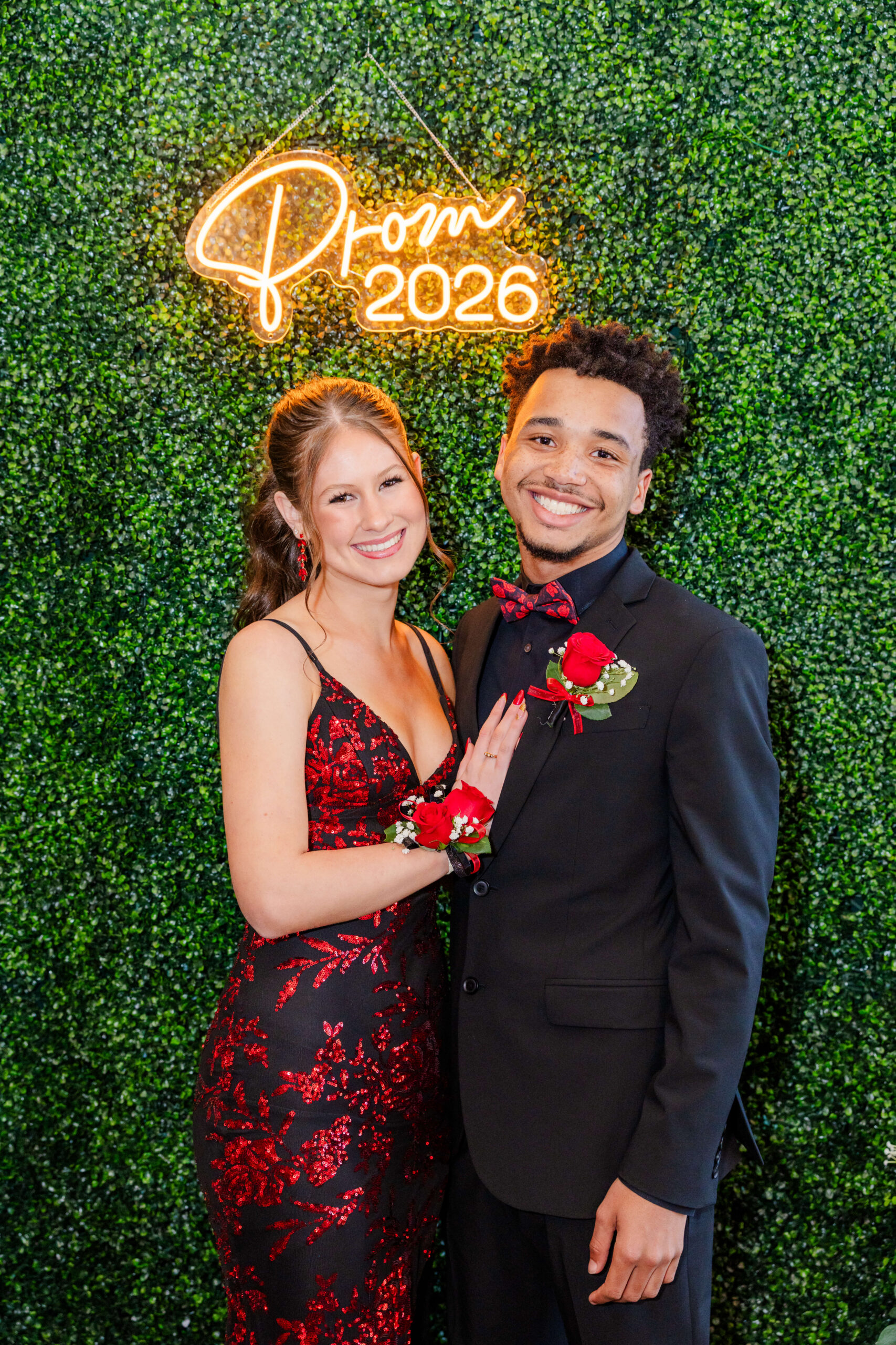 A woman in a red dress smiles while standing with her prom date in his black tux rental in michigan