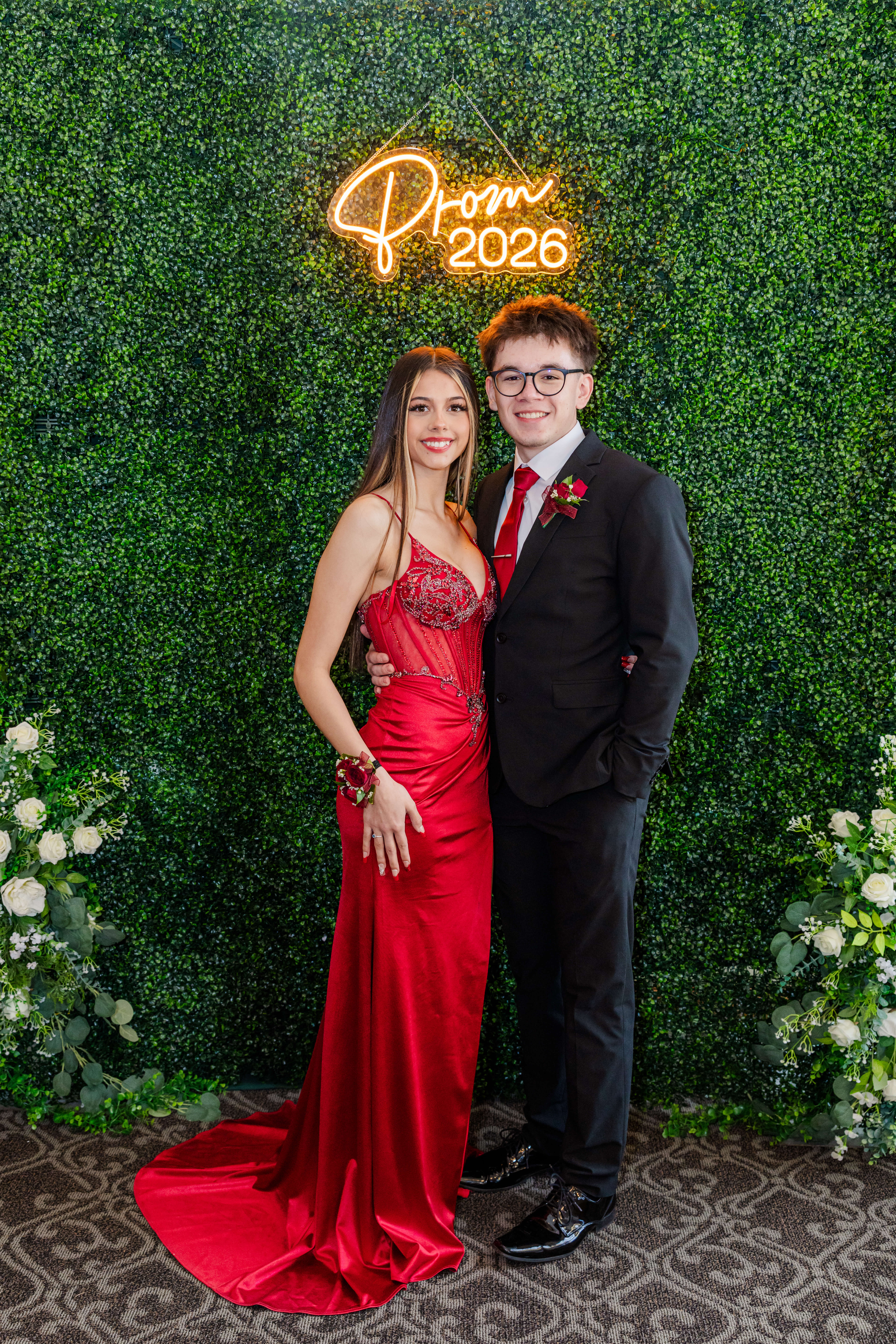 Happy high school senior in red and black stand under a prom 2025 neon sign after finding tux rental in michigan