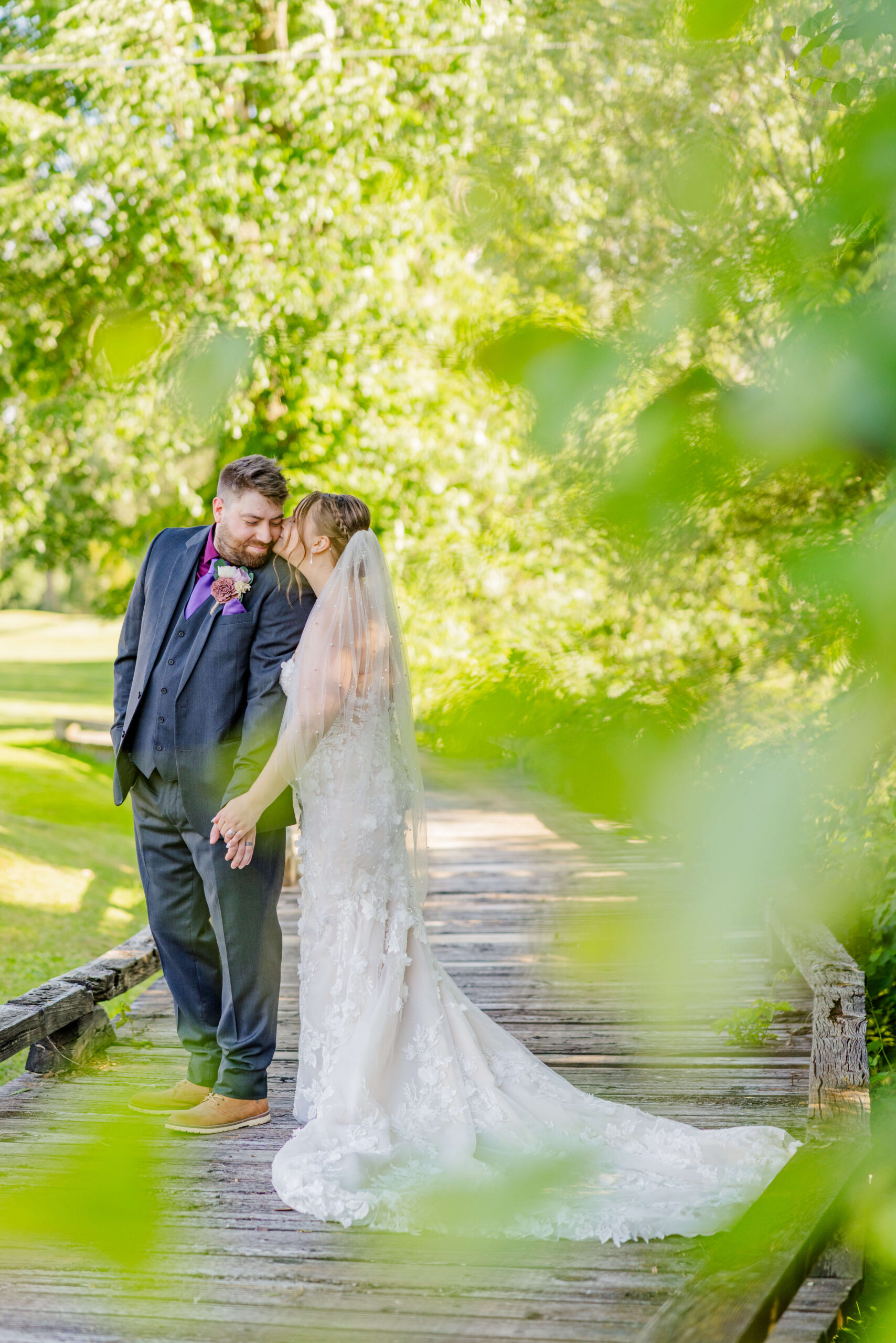 A happy newlywed couple kiss while standing on an old wooden bridge during their lapeer country club wedding