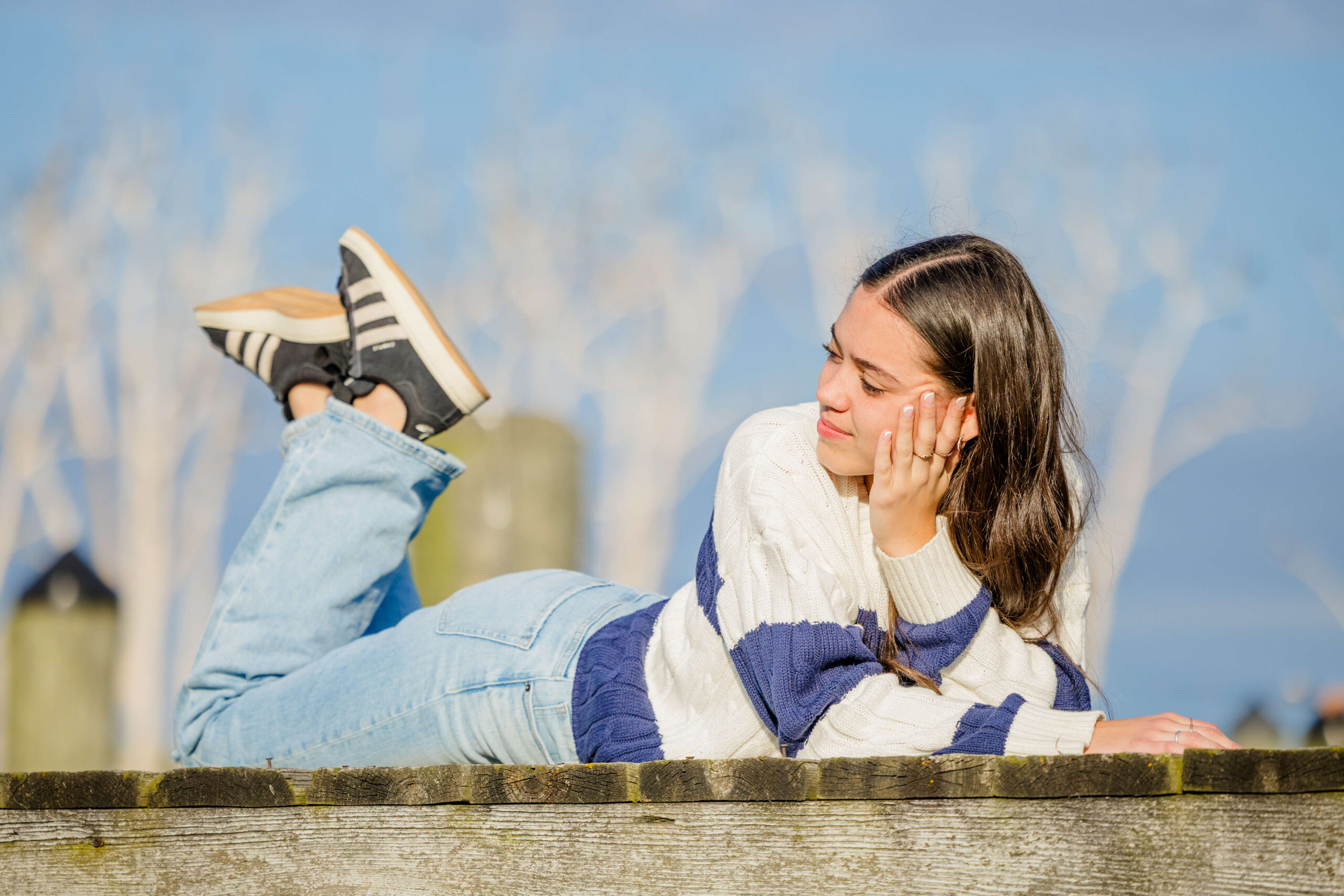 A high school senior in a white and blue stripe sweater lays across a dock at sunset after visiting nail salons in michigan