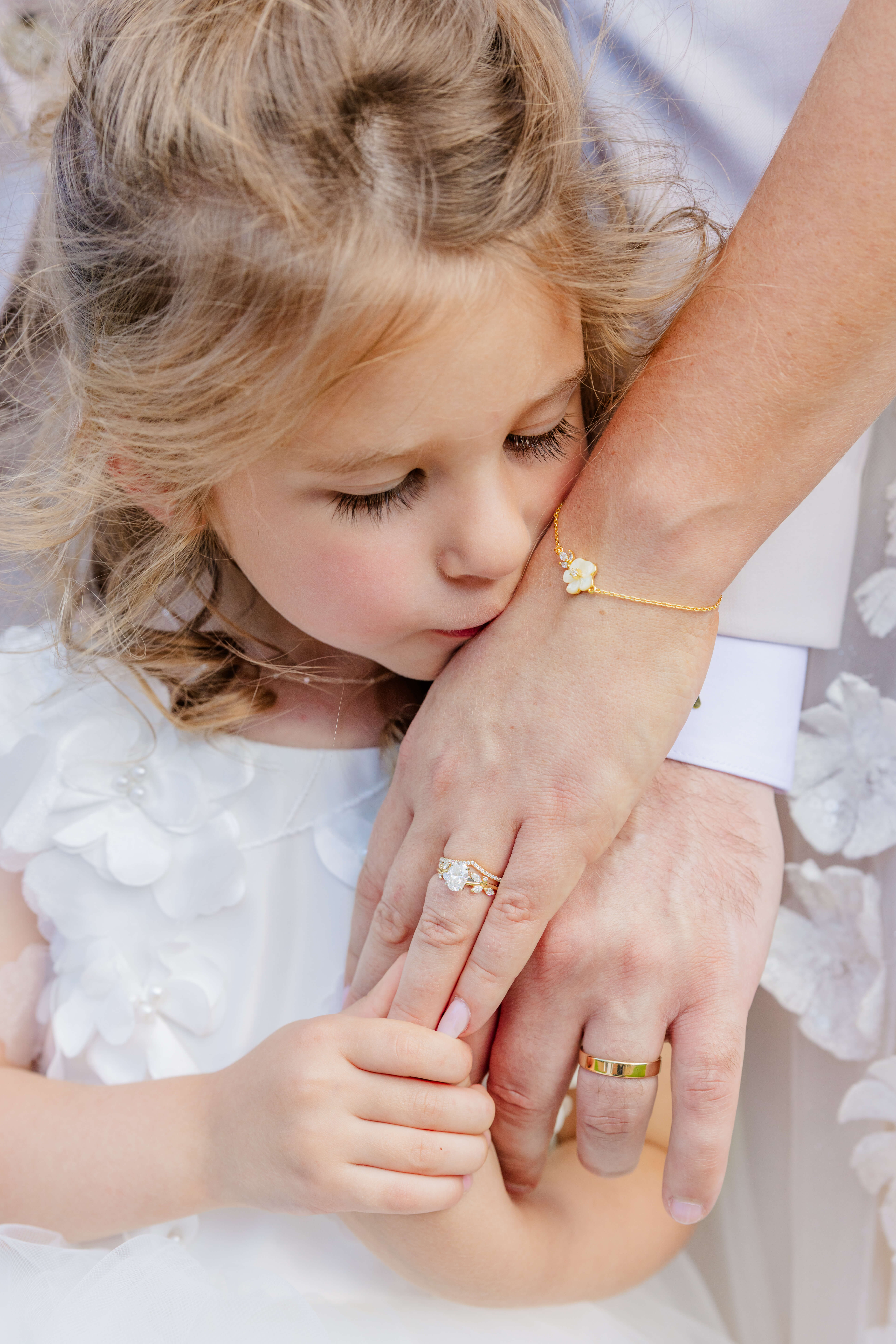 A young girl kisses mom's hand while standing in a white flower girl dress during an oakhurst country club wedding