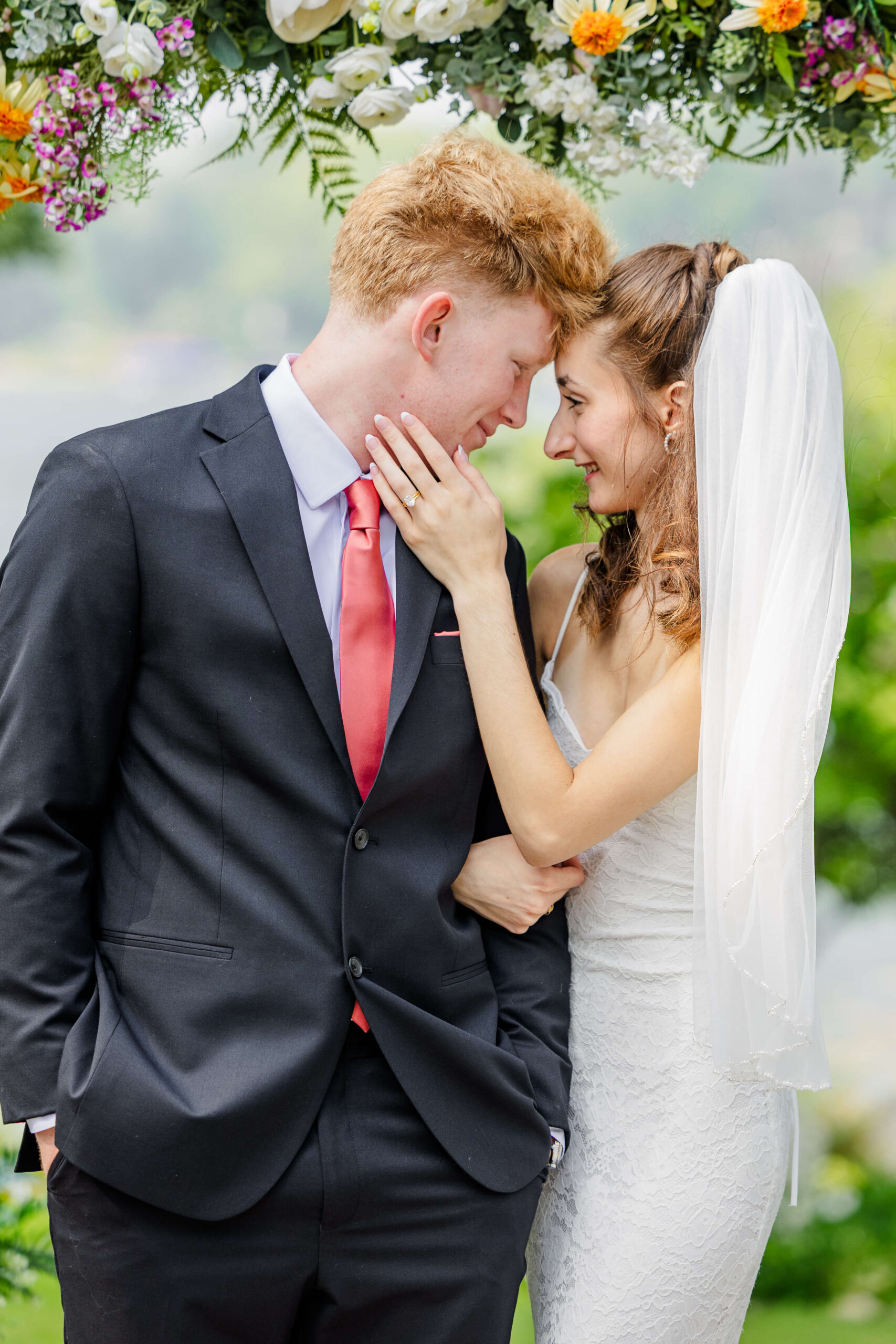 Happy newlyweds snuggle under a floral arch touching foreheads during their Royal Park Hotel wedding