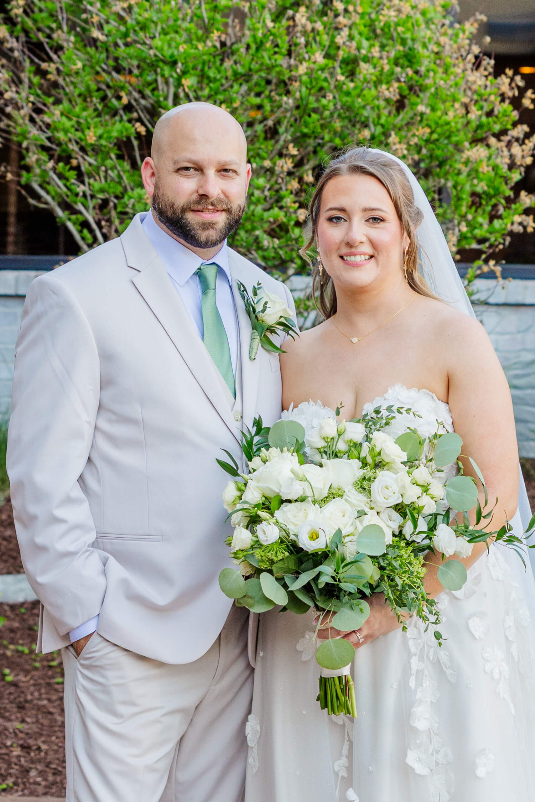 A bride and groom stand smiling together while holding the large white bouquet during their meadow brook hall wedding