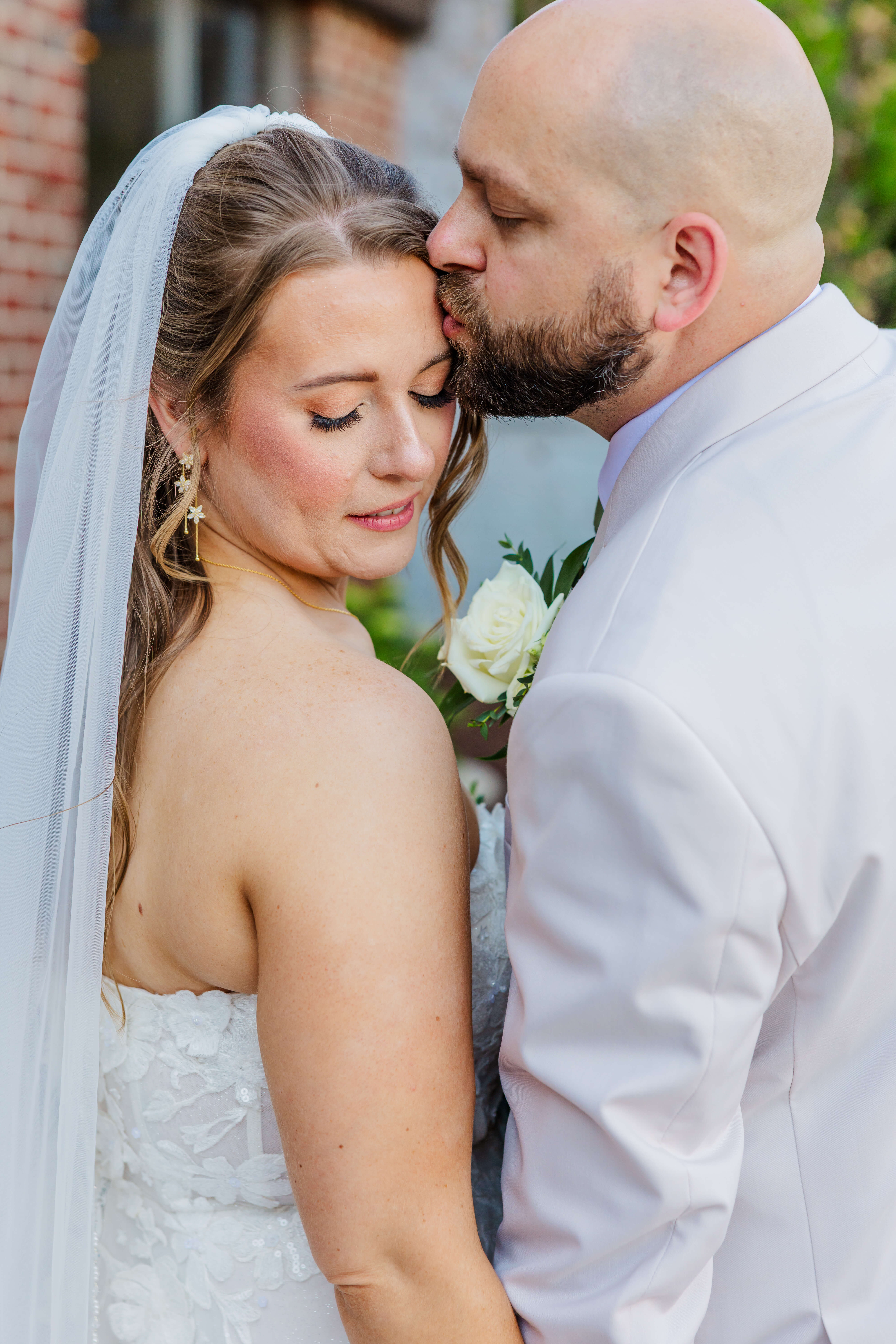 A groom in grey kisses the forehead of his bride during their meadow brook hall wedding